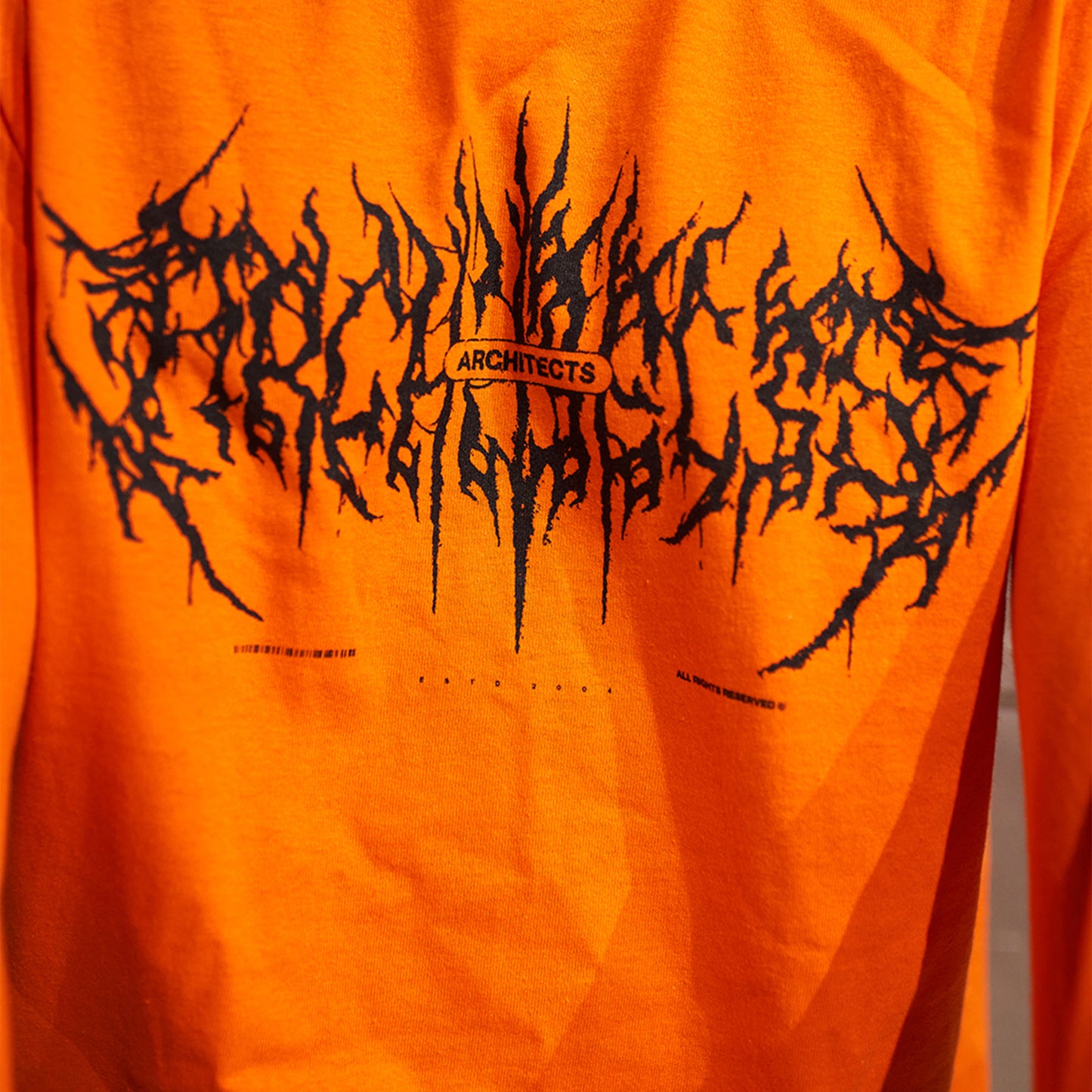 Orange long-sleeve T-shirt featuring a Barbed Wire Architects print across the front and along the sleeves