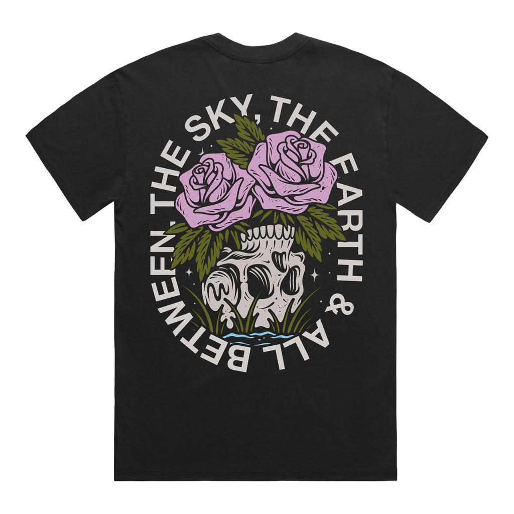 Back of a black short-sleeve t-shirt featuring a flower–skull graphic, with white text around it that reads “The Sky, The Earth & All Between.”