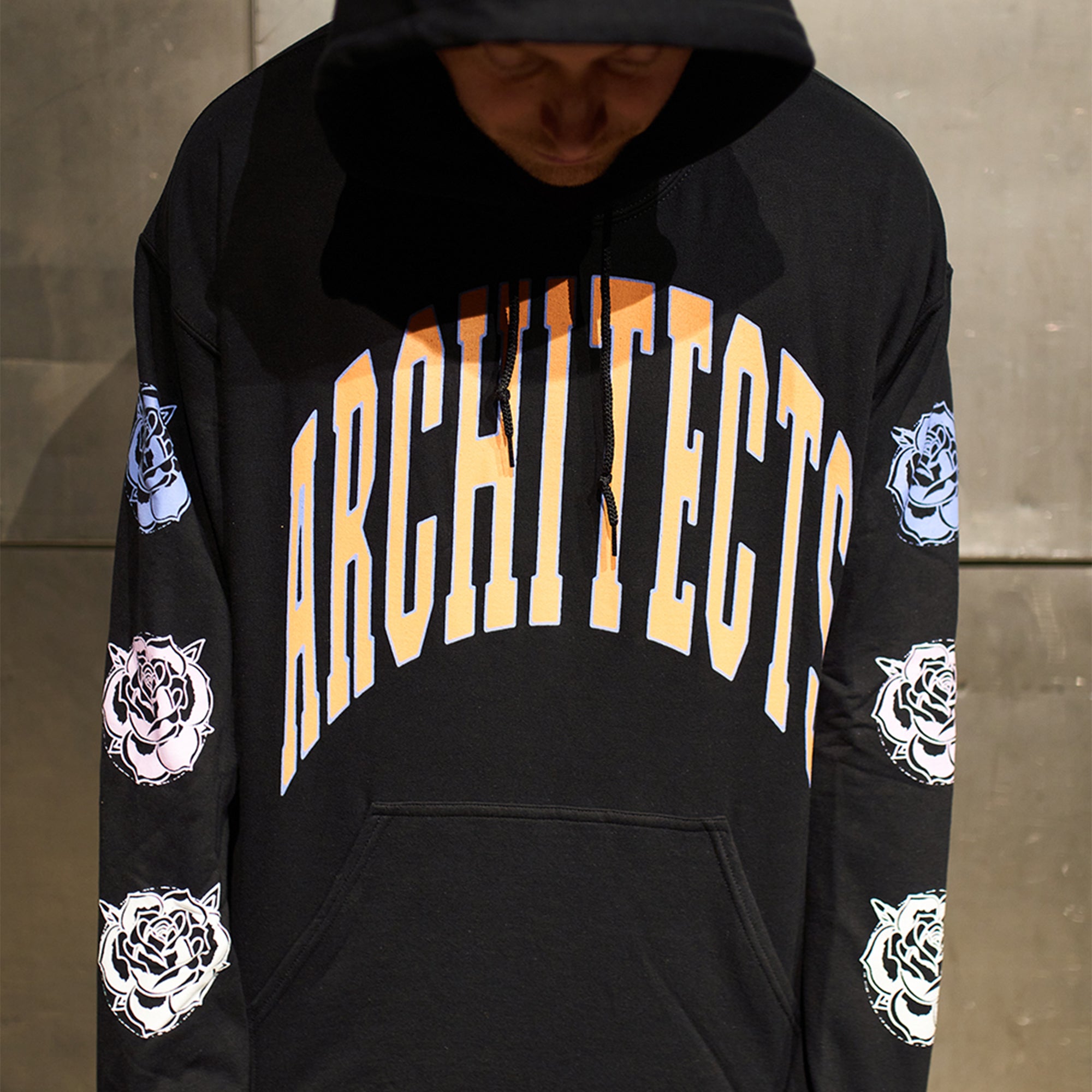 Black regular-fit unisex hoodie featuring an orange Architects print across the front, with blue, pink, and white rose prints along the sleeves.