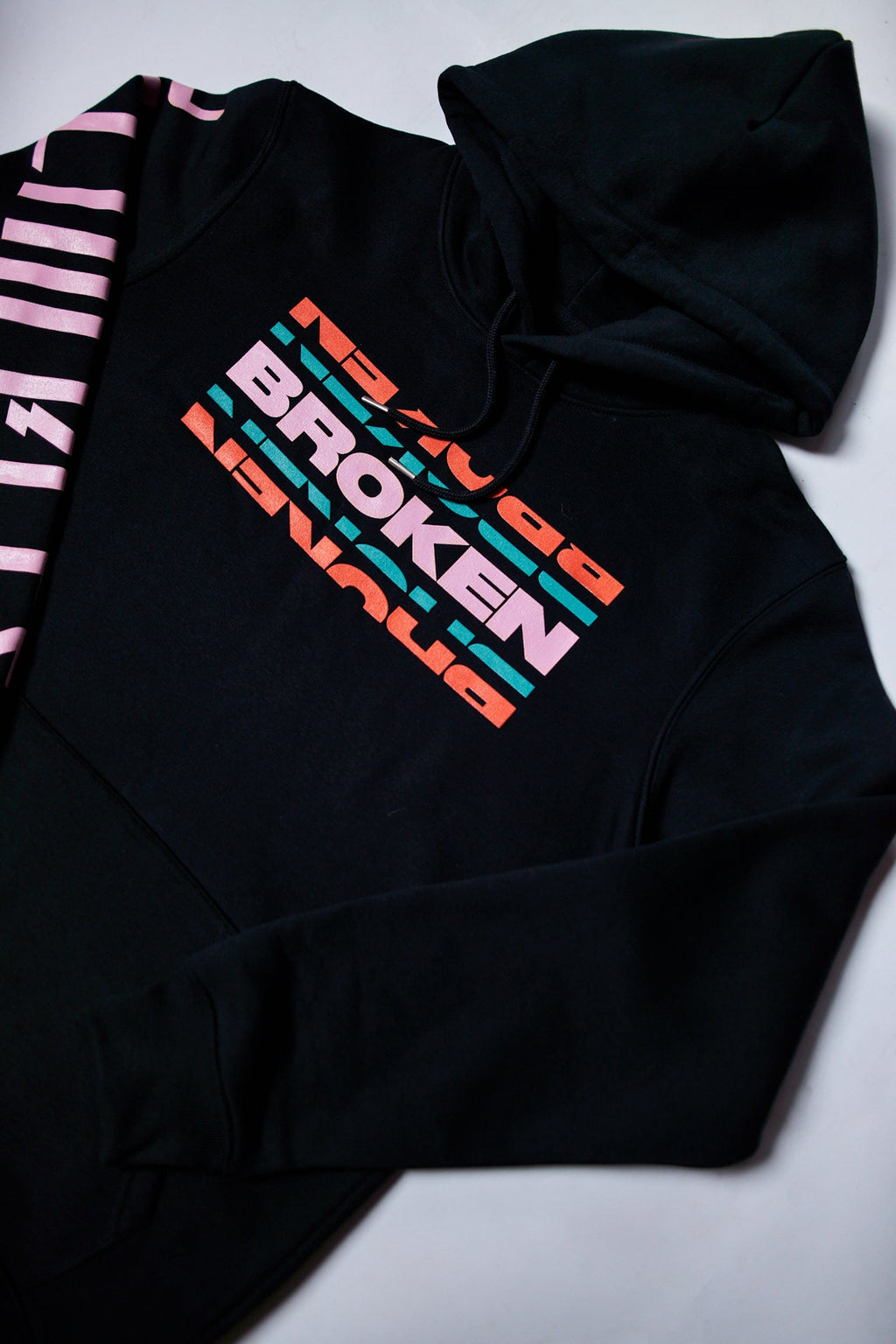 Black unisex hoodie featuring a colourful 'Broken' text print across the front and a pink Architects logo print along the sleeve.