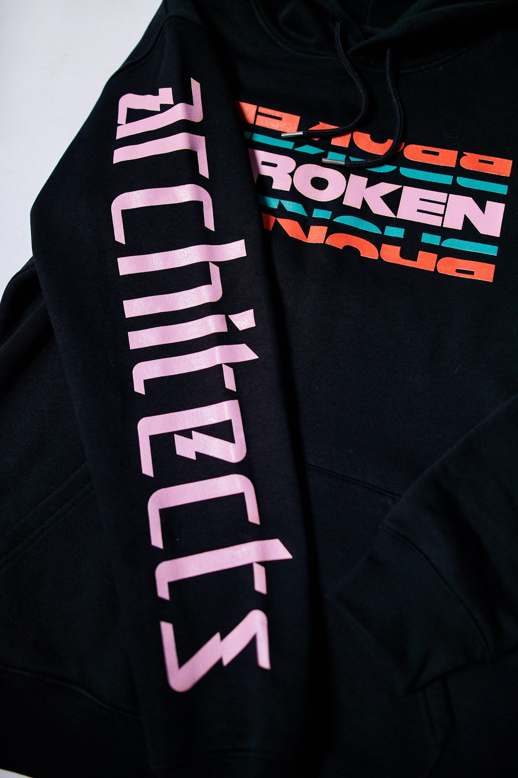 Black unisex hoodie featuring a colourful 'Broken' text print across the front and a pink Architects logo print along the sleeve.