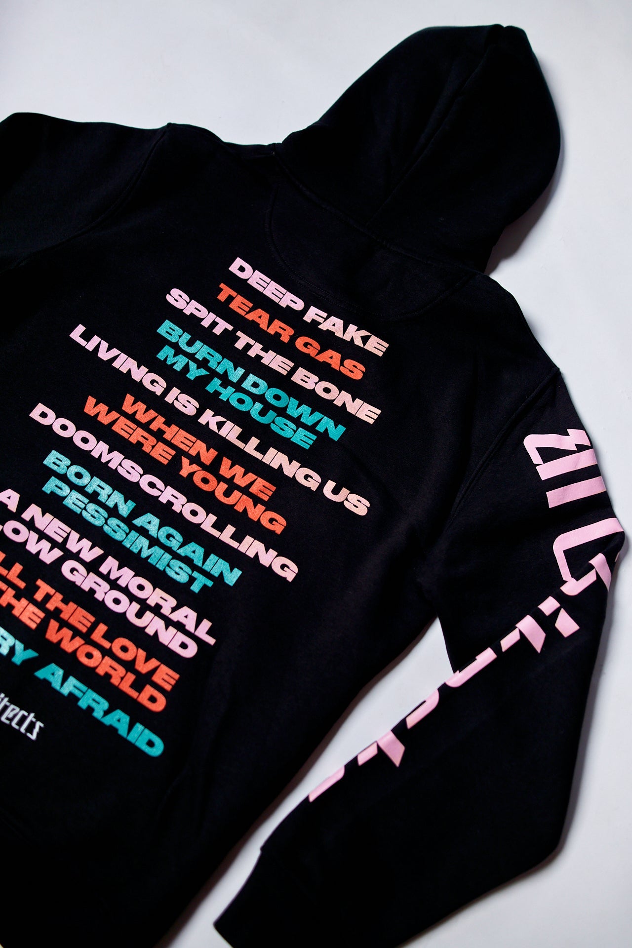 Black unisex hoodie featuring a colourful 'Broken' text print across the front and a pink Architects logo print along the sleeve.